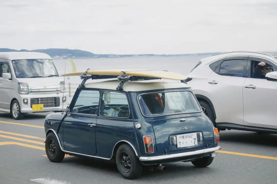海沿いの道に停められた、サーフボードを積んだクラシックなミニクーパー