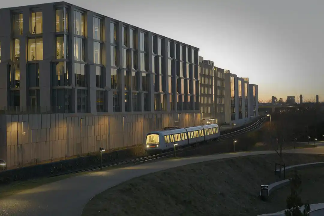 一列現代化的丹麥城市列車在黃昏時分駛過菲特烈堡地區,背景是亮起燈光的城市建築。