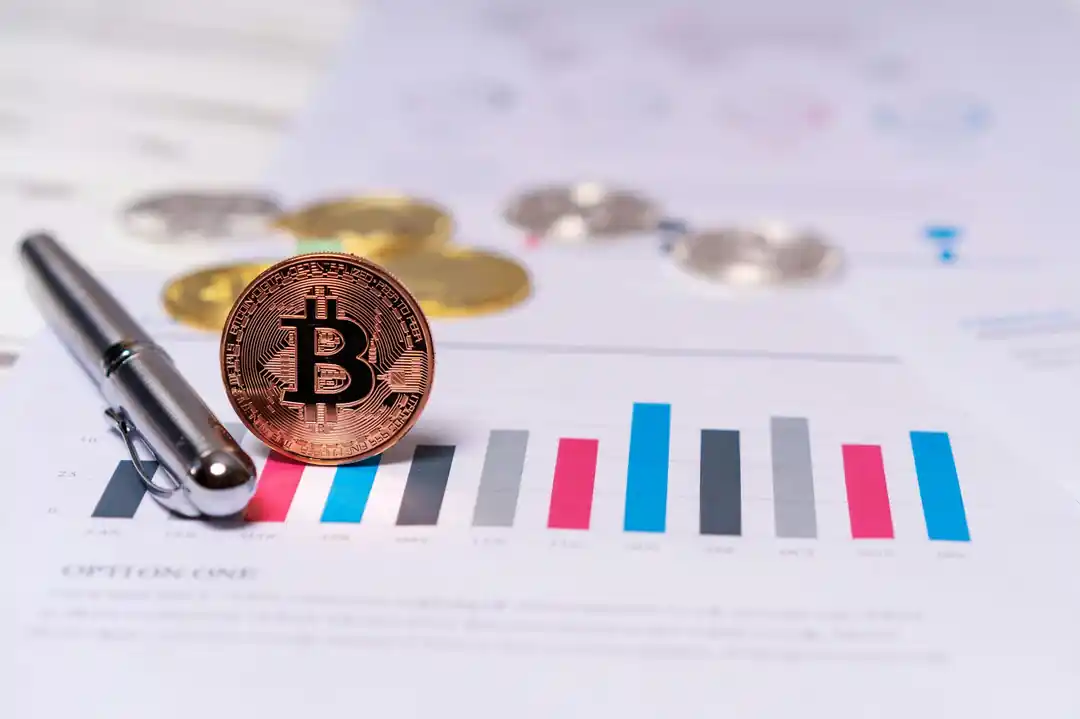 金融チャートの上に置かれたビットコインのコインとペン