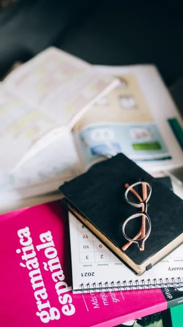 A study setup with a Spanish grammar book, calendar, and eyeglasses on a desk, suggesting focused learning.