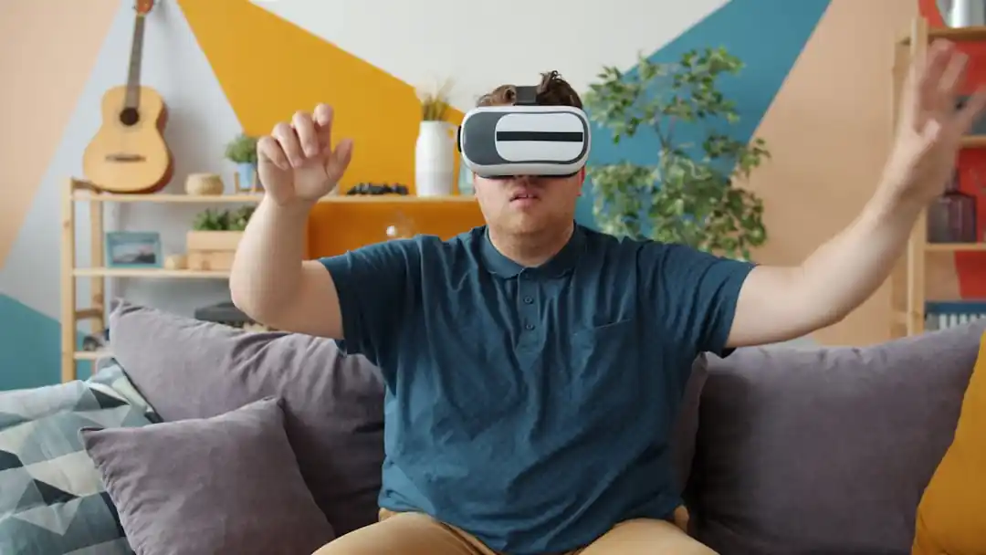 一名年輕男子戴著VR頭盔,坐在沙發上,雙手在空中進行互動操作。