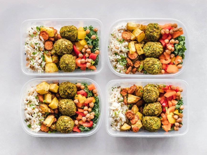 Meal prep containers filled with rice, chickpeas, falafel, and vegetables.