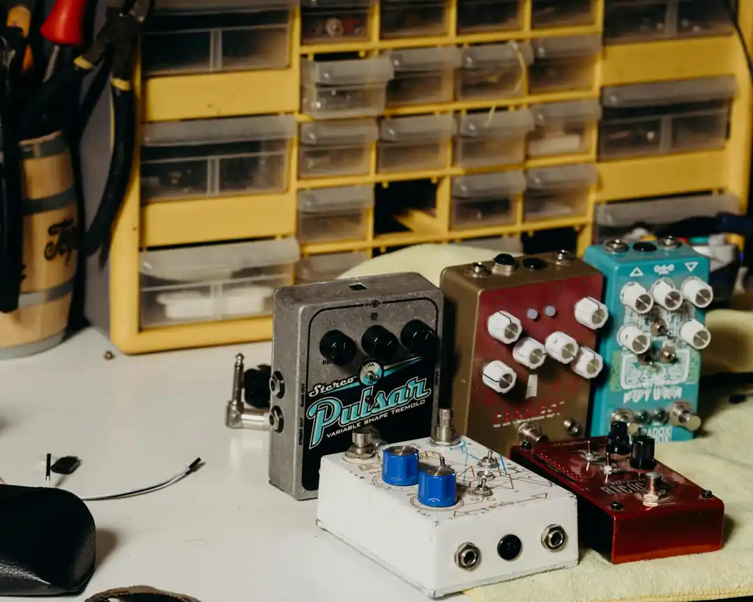 A workbench with several guitar effects pedals in various states of assembly, showing their internal circuits.