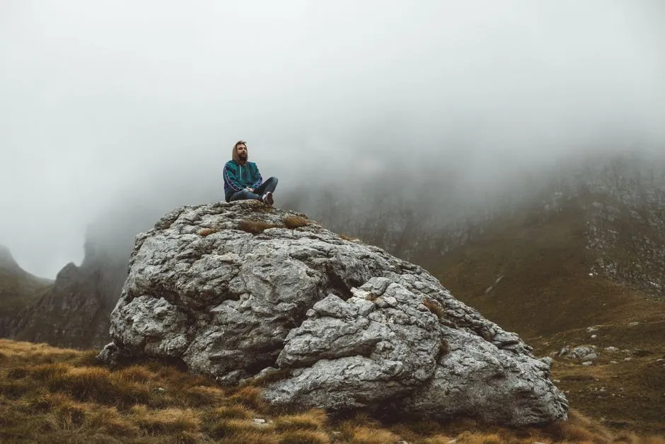 A contemplative man sitting on a rock amidst misty mountains