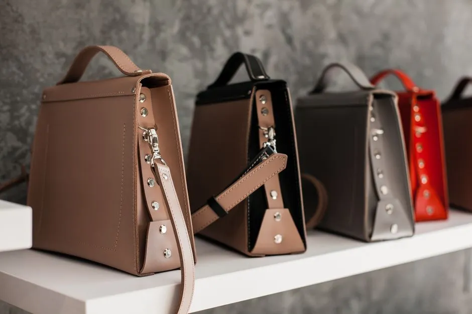 A collection of minimalist leather handbags in various colors arranged on a white shelf.