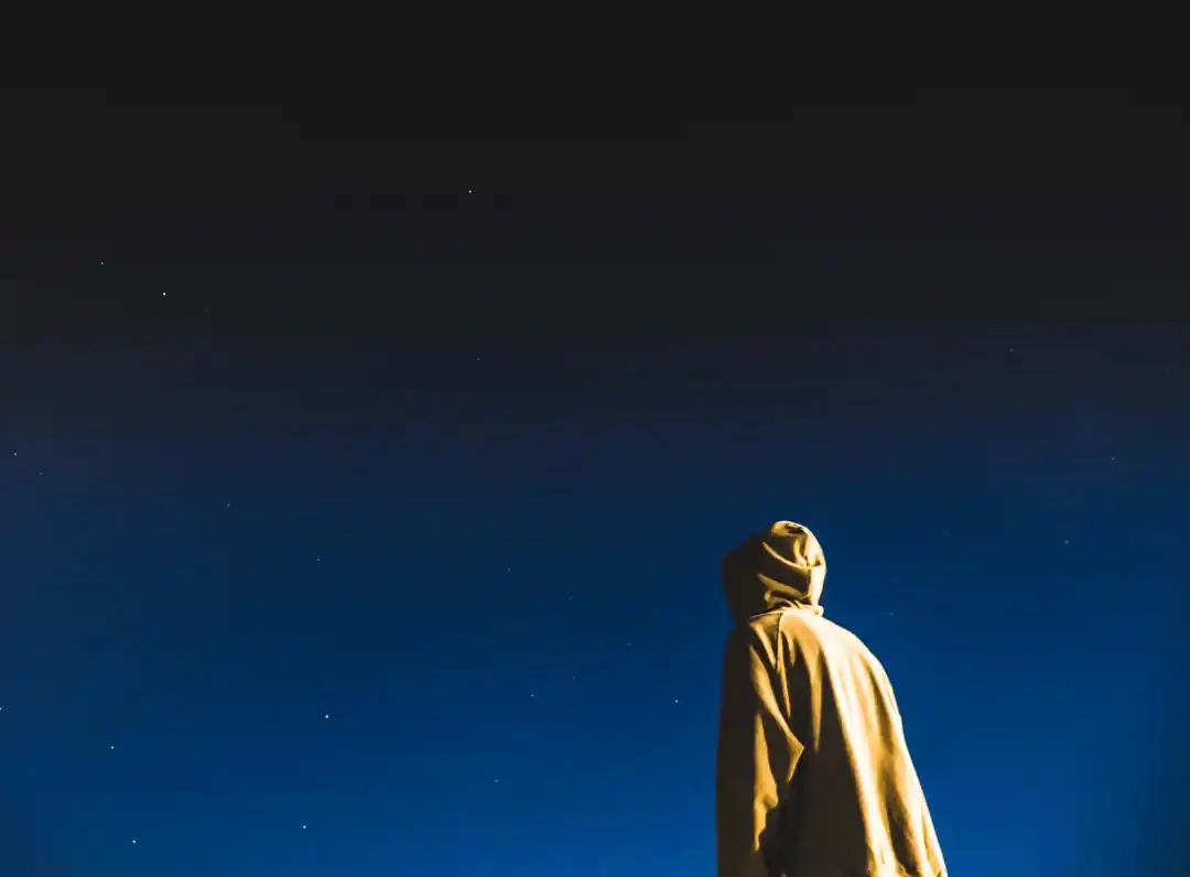 パーカーを着た人物が、夜空の星々を見上げている後ろ姿
