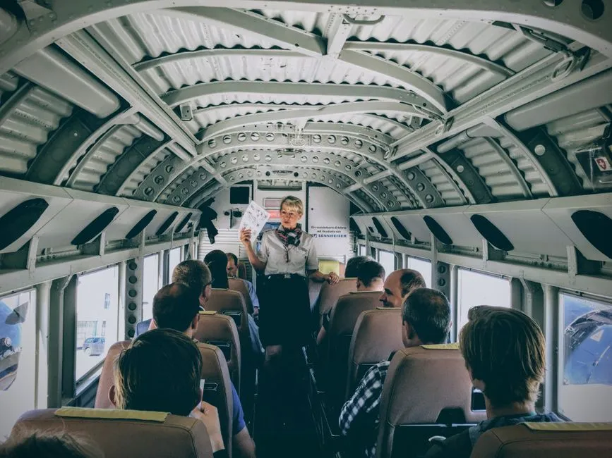 A flight attendant demonstrating safety procedures to passengers inside a vintage plane.