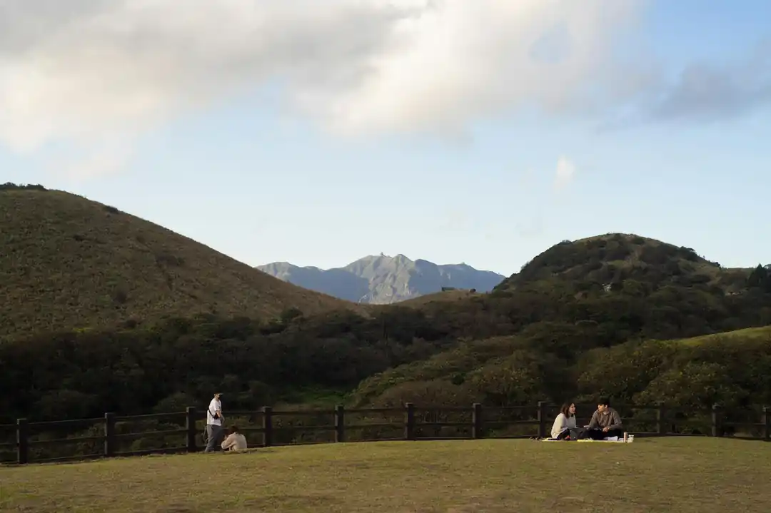 遊客在陽明山擎天崗的草原上野餐,遠方是連綿的山景。