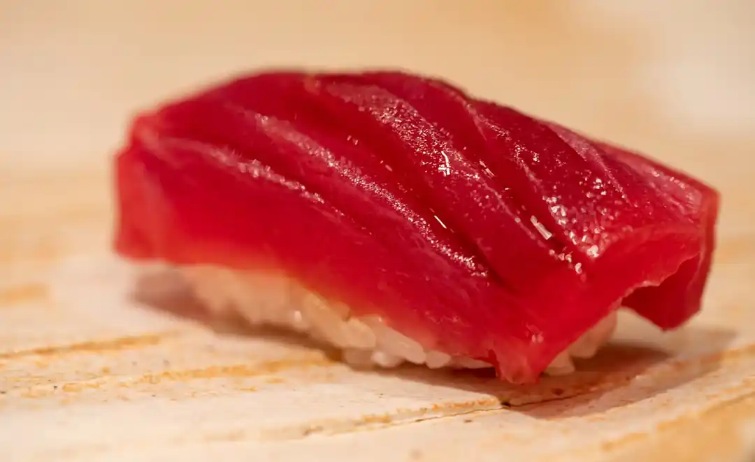 木製のテーブルの上に置かれた、一切れのマグロの寿司