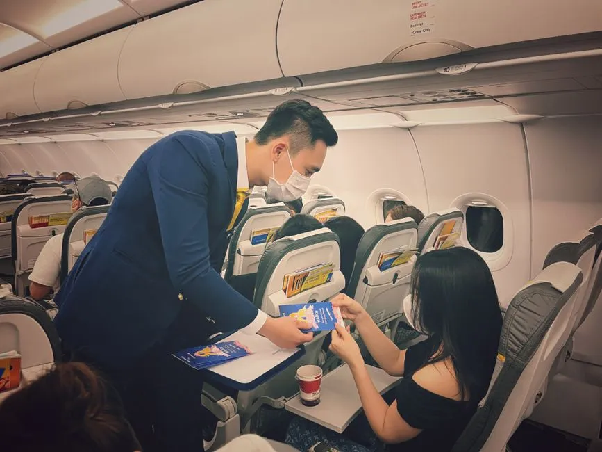 A flight attendant wearing a protective mask while attending to passengers in an aircraft cabin.