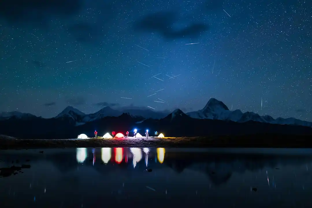 湖のほとりでテントを張り、満天の星と流星群を眺める人々