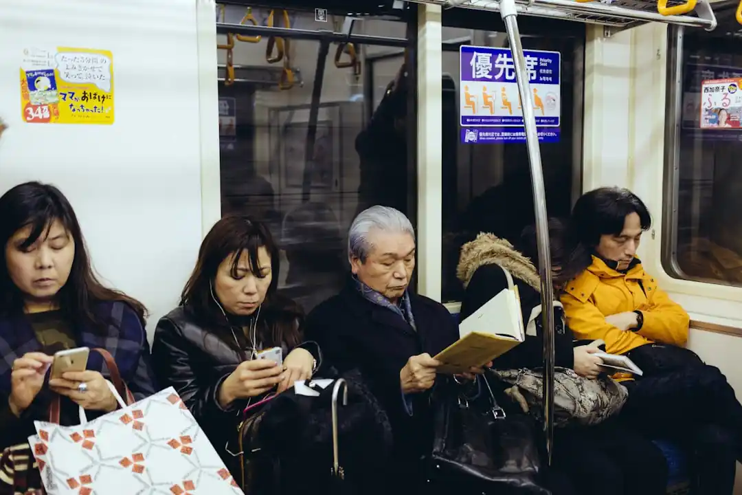 電車内で座っている人々。それぞれがスマホを見たり本を読んだりしている。