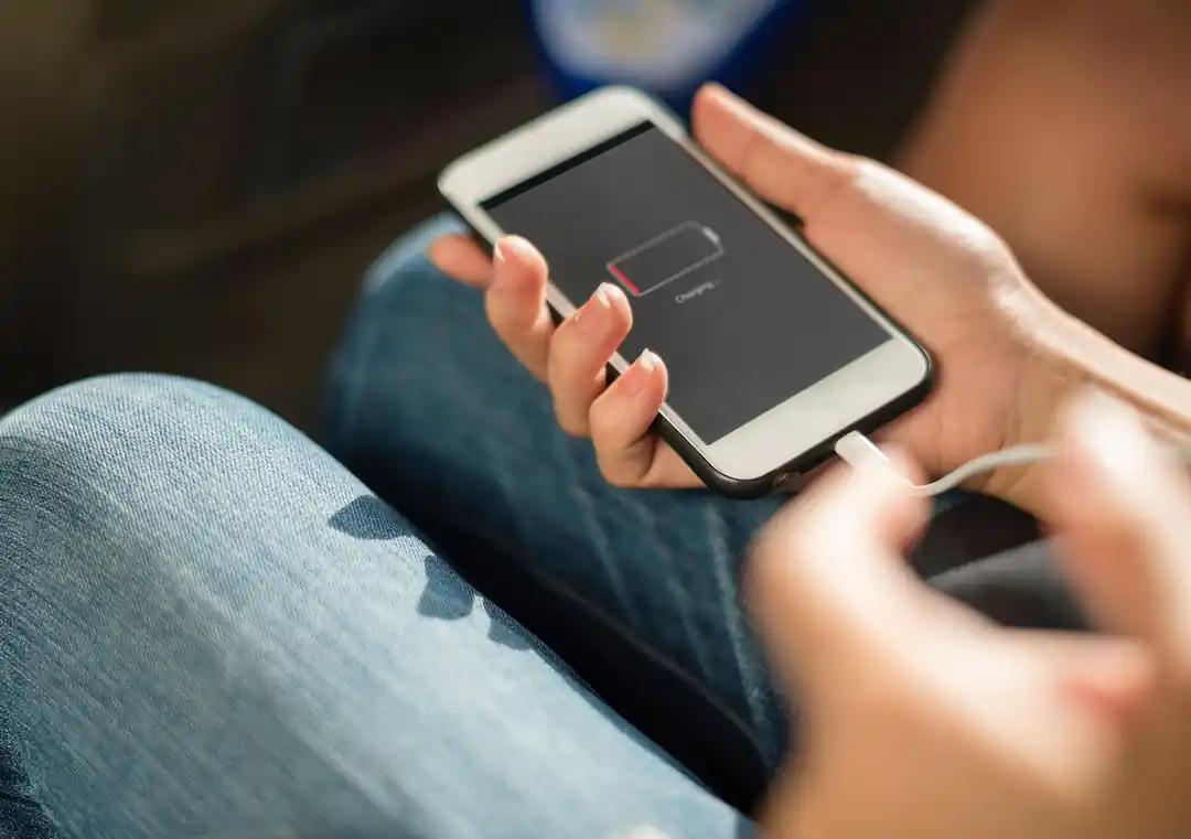 手に持たれたスマートフォンに充電ケーブルが接続されている様子