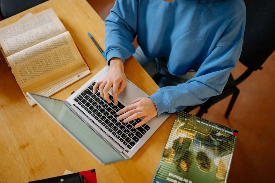 開いた本に囲まれながら、リサーチや課題に集中してノートパソコンを操作する学生
