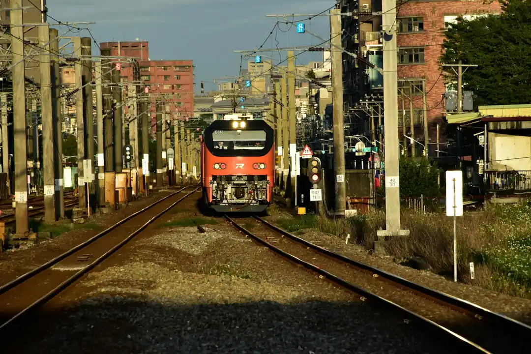 一輛高雄輕軌列車在陽光下沿著海岸線行駛,背景是藍天白雲和城市建築。