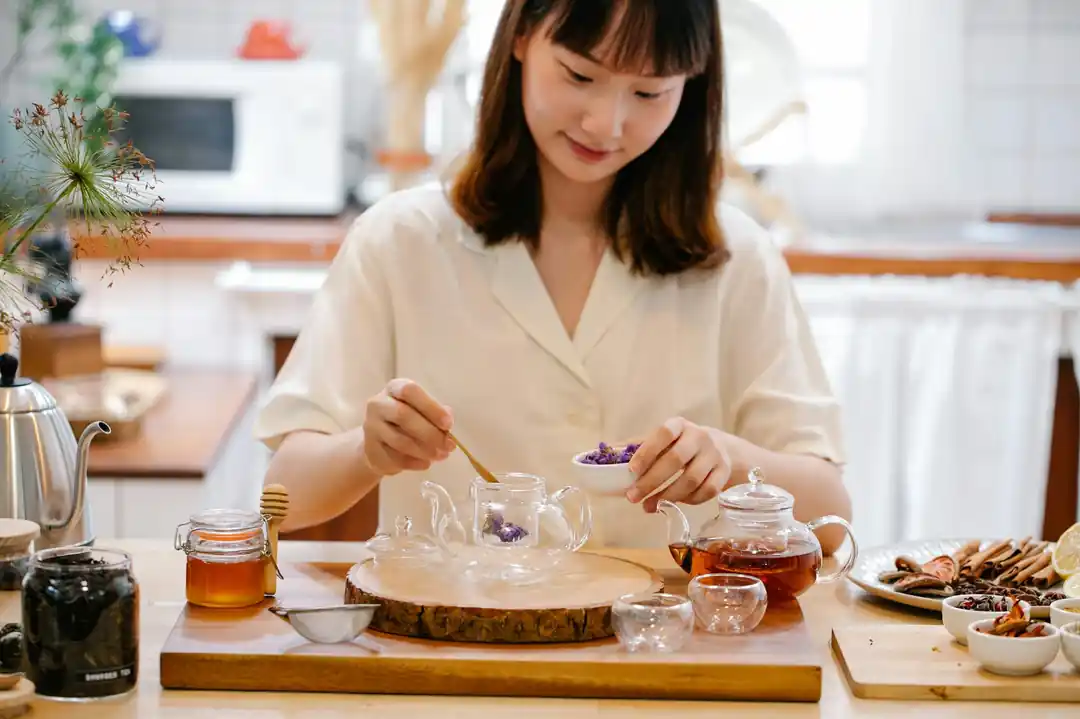 一位亞洲女性在溫暖的廚房裡,正在準備帶有香料的草本茶。