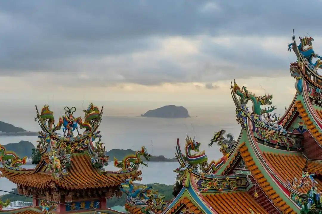 雕刻精細的廟宇屋頂,龍的雕像在多雲的天空下俯瞰著寧靜的海洋。