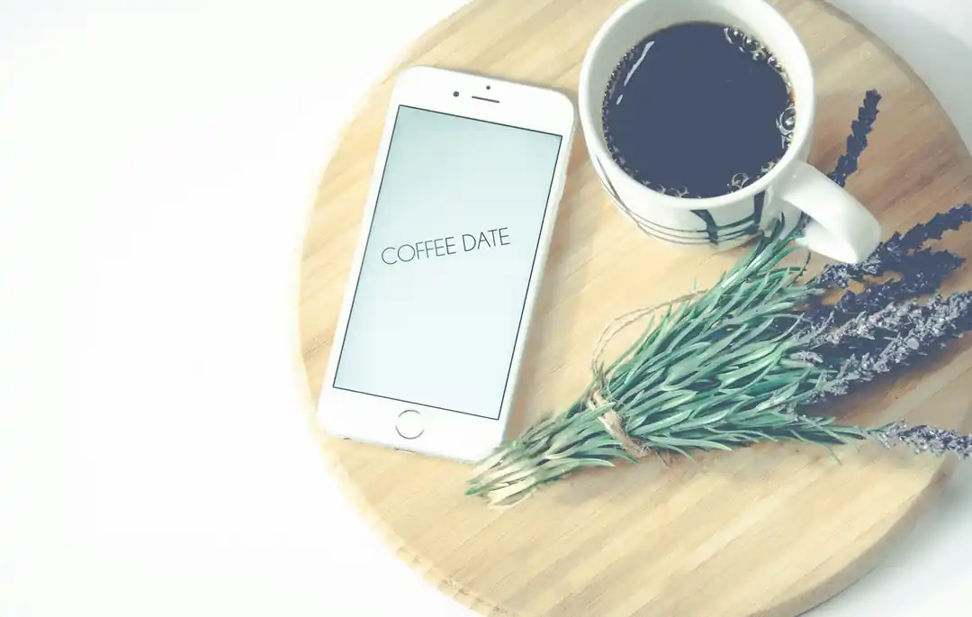 木製托盤上放著一杯咖啡、幾支薰衣草和一部顯示著「Coffee Date」字樣的智慧型手機。
