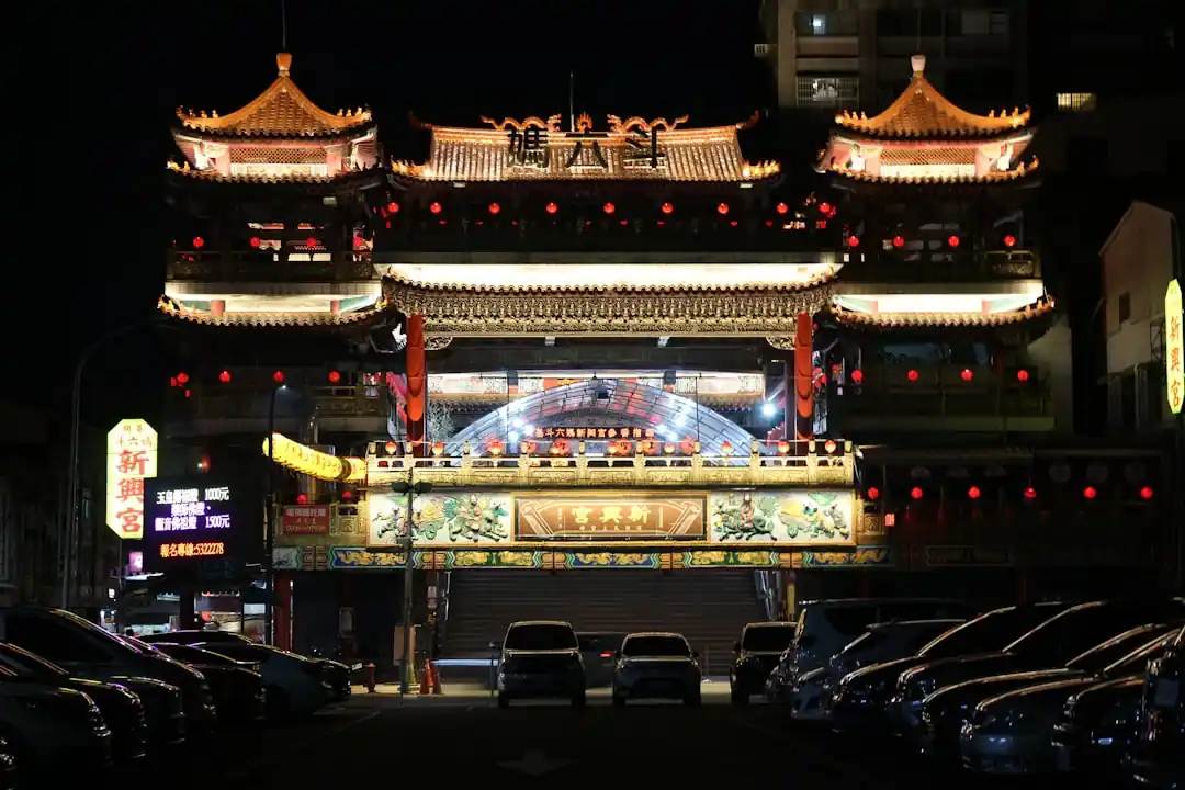 一座台灣傳統廟宇在夜晚燈火通明,前方停著幾輛汽車。