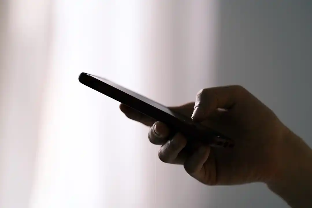 一隻手正拿著一支黑色的智慧型手機,螢幕上顯示著訊息,但內容模糊不清。