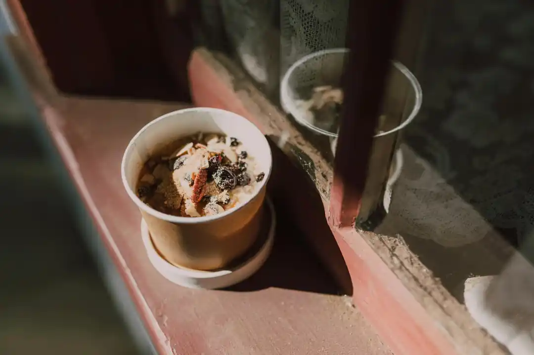 一碗盛裝著水果和堅果的燕麥粥,旁邊的窗戶透進溫暖的晨光。