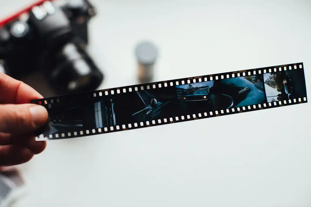 ヴィンテージカメラを背景に、古いフィルムのネガを持っている手。
