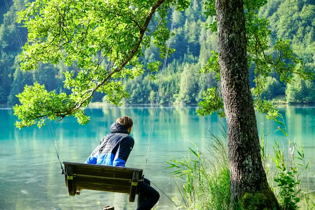 湖のほとりのブランコに座って景色を眺めている女性