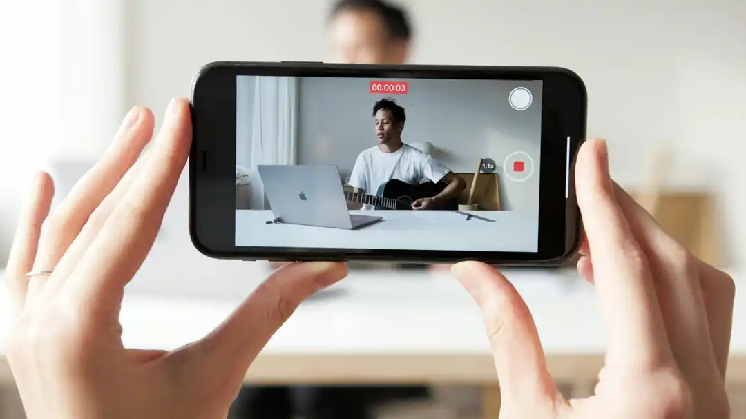 スマートフォンを三脚に固定し、ギターを弾きながら歌う男性。