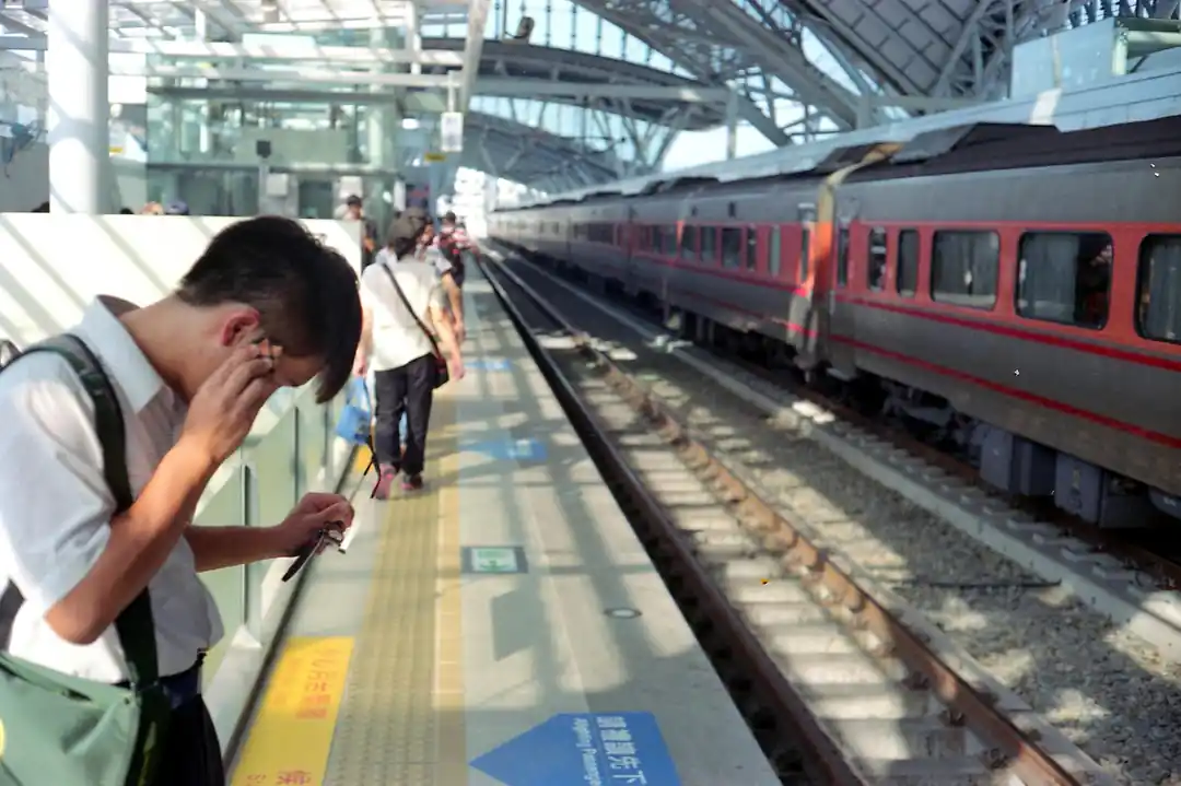 通勤者們在台中火車站的月台上等車,一列紅白相間的火車停靠在旁。