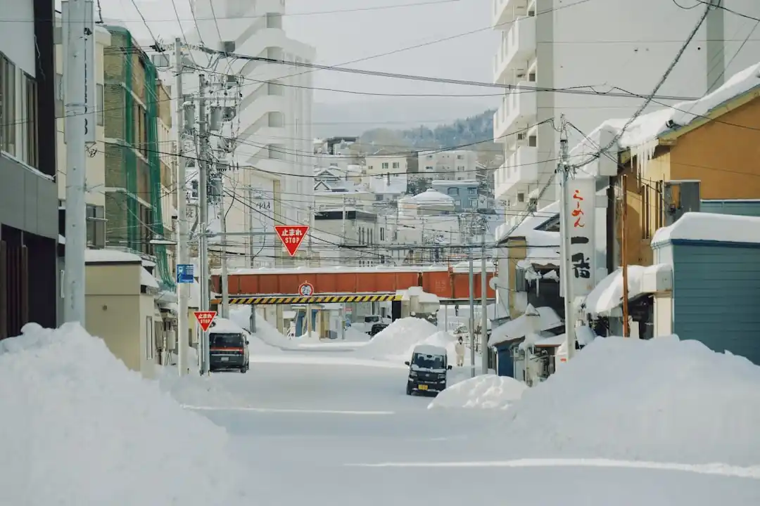 雪が積もる日本の伝統的な温泉街。ガス灯が灯り、川には橋がかかっている。