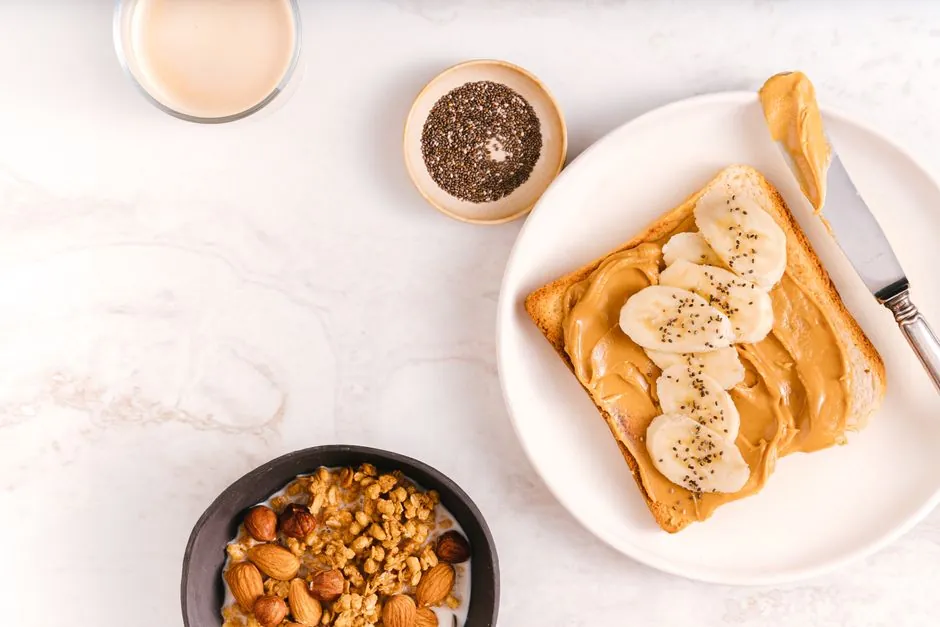 A beautifully arranged morning light breakfast with banana toast, nuts, and chia seeds on marble.