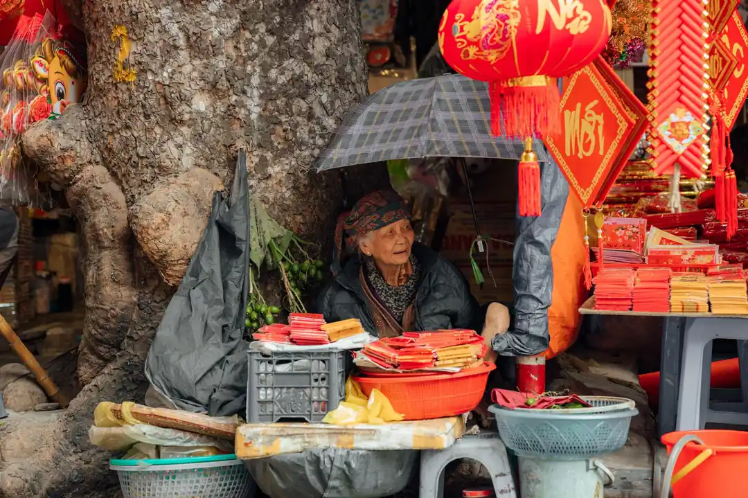 一位年長的婦女在她的攤位上,販售著各式色彩鮮豔的農曆新年裝飾品。