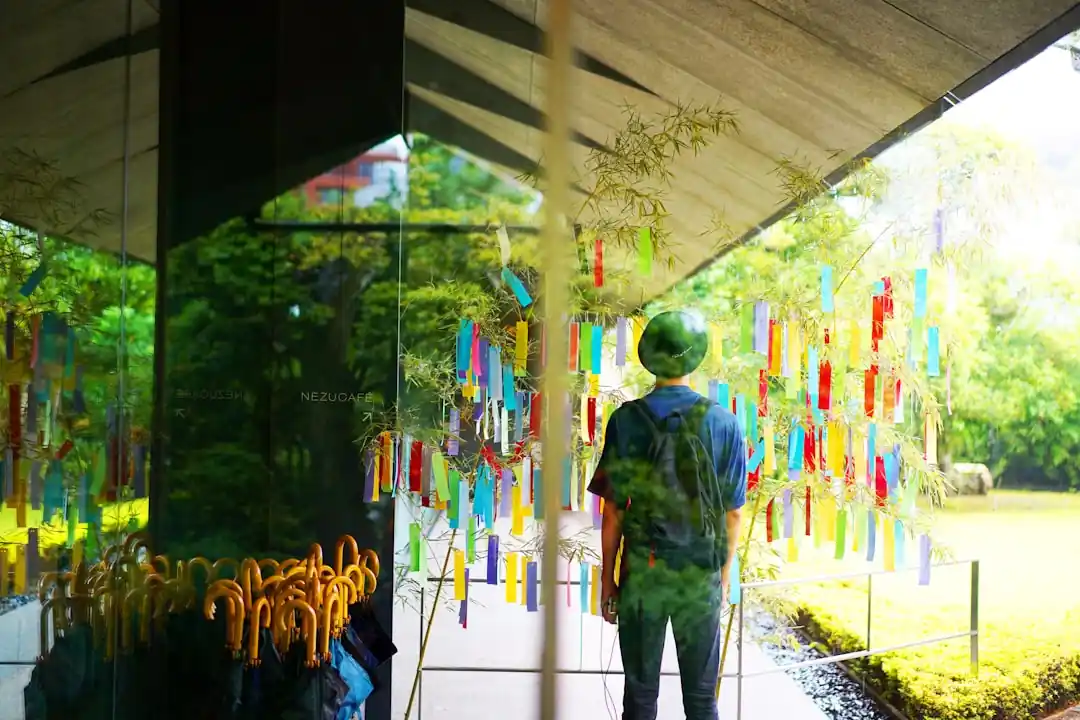 美術館のガラス窓の前に立ち、外の竹のアートインスタレーションを眺める男性