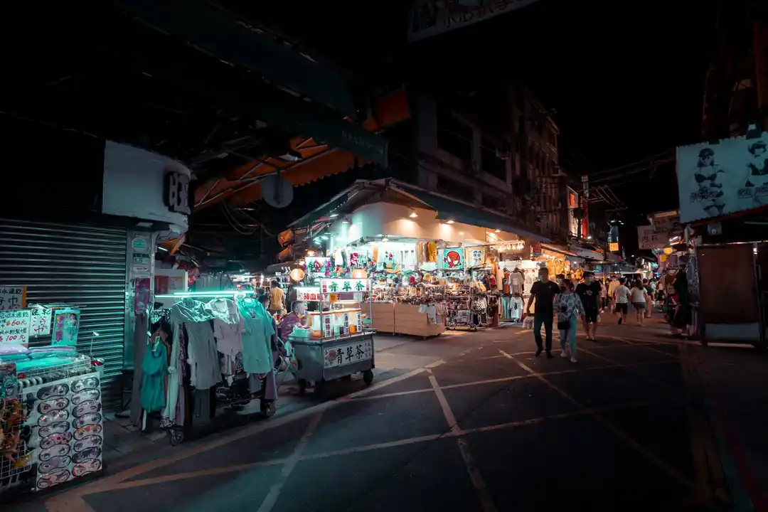 夜晚的夜市攤位,掛著發光的燈籠,前方有許多排隊的人潮。