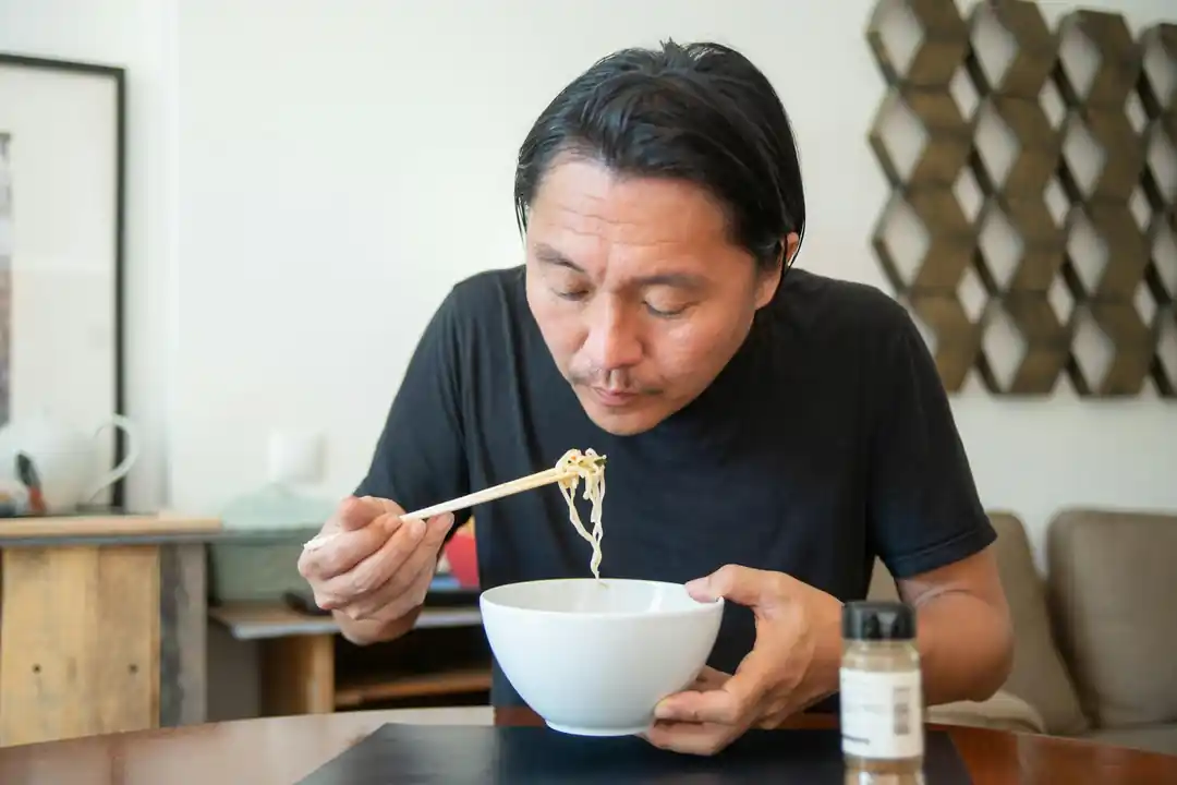 アジア人の男性が屋内で箸を使って麺を食べている