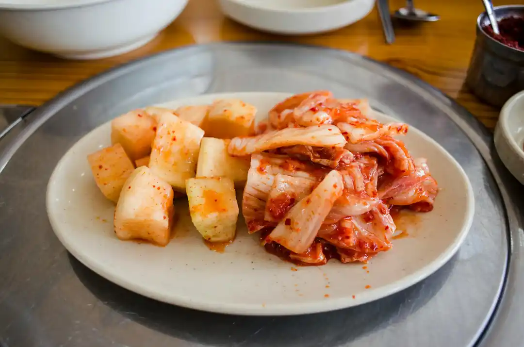 흰 접시 위에 먹음직스럽게 담긴 배추김치와 깍두기 클로즈업 사진.