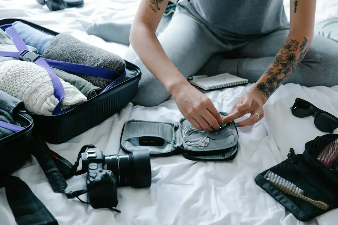旅行の準備のため、スーツケースとイヤホンや充電器などの電子機器をパッキングしているタトゥーのある女性