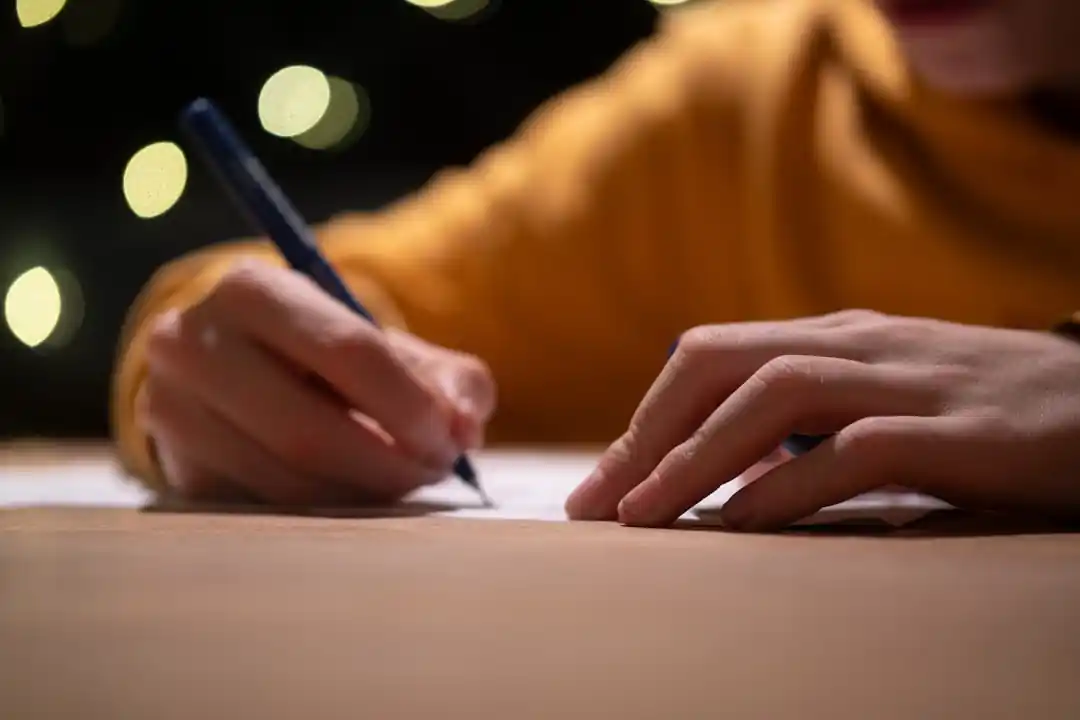 ペンを持って、紙に何かを書いている人の手元。