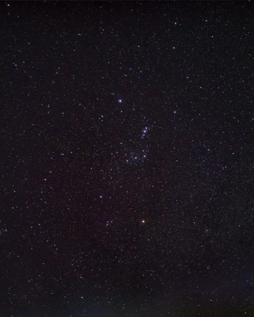 The bright stars of the Orion constellation glowing distinctly against a crowded field of cosmic dust and stars