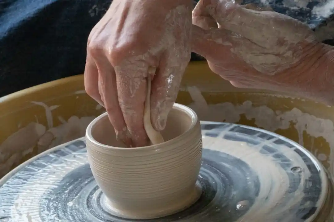 ろくろの上で白い陶器の器を丁寧に作る人の手元。