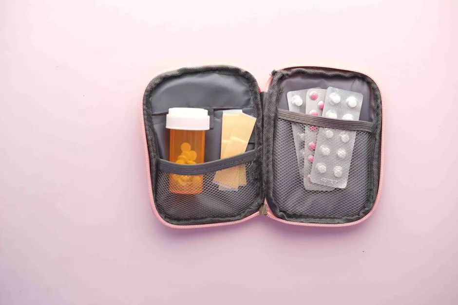 An open first aid kit with a pill bottle, blister packs, and bandages on a pastel background.