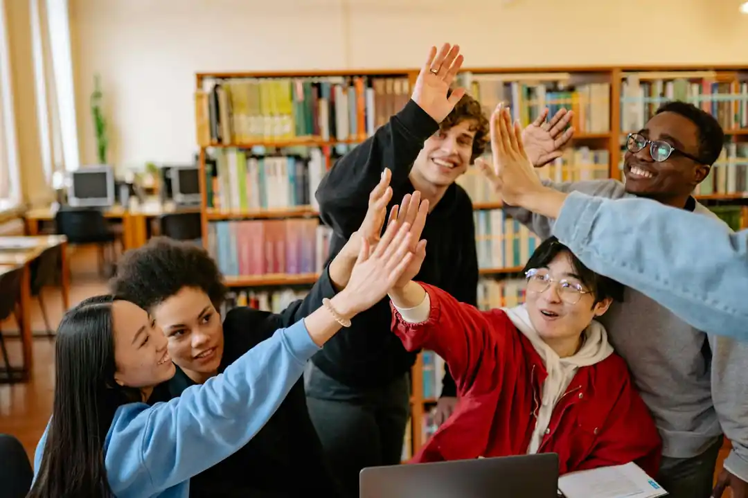 도서관에서 함께 공부하던 여러 학생들이 성공적으로 과제를 마친 후 다 함께 하이파이브를 하고 있다.