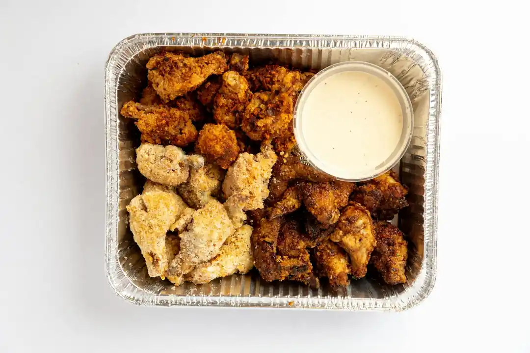 A foil container filled with homemade chicken nuggets and a small cup of dipping sauce.