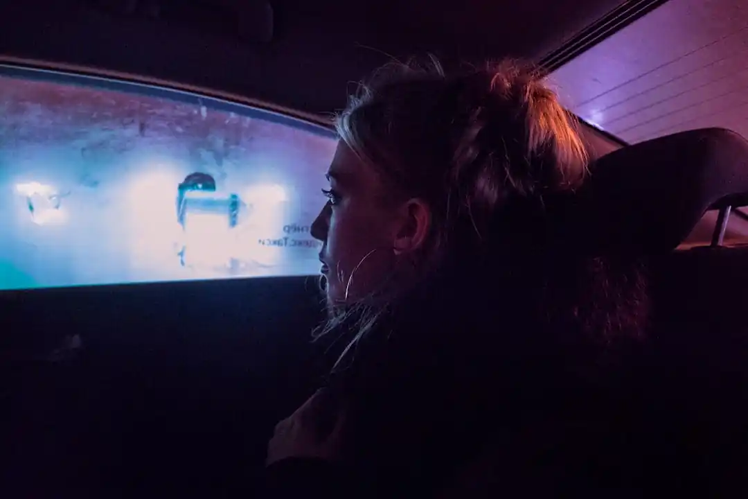 一位女性坐在計程車後座,專注地看著她的手機,窗外的夜景流逝。