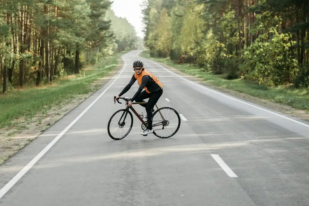 一位穿著橘色背心的自行車騎士,在充滿綠色植物的森林道路上騎行。