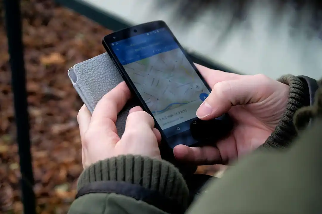 一雙手在戶外拿著智慧型手機,螢幕上顯示著地圖 App 的導航畫面。