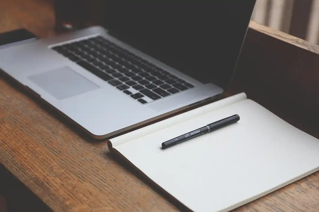A clean, organized home office desk with a laptop, notebook, and pen, suggesting a focused work environment.