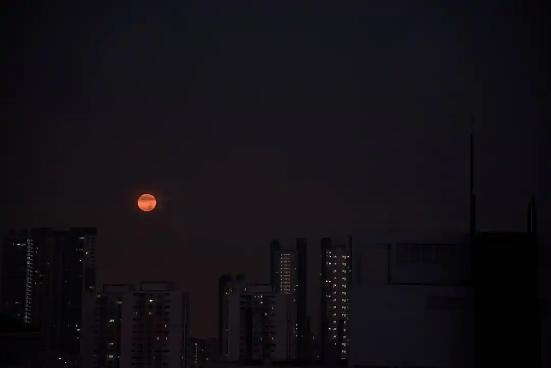 夜の都会のビル群の上に輝く満月