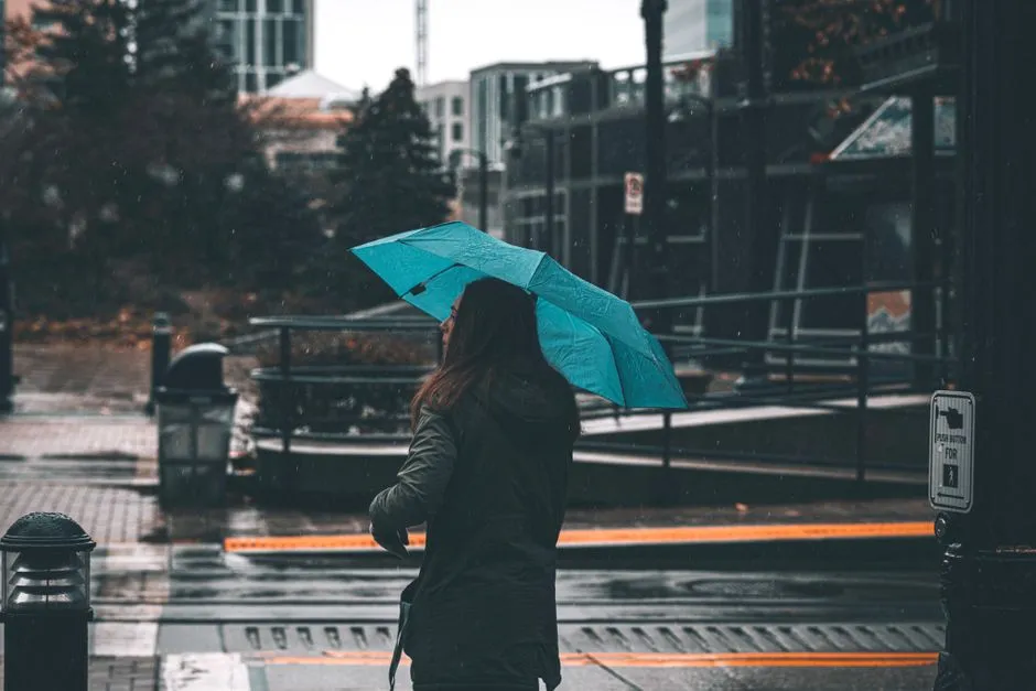 一名女子撐著藍色雨傘走在雨天的城市街道上