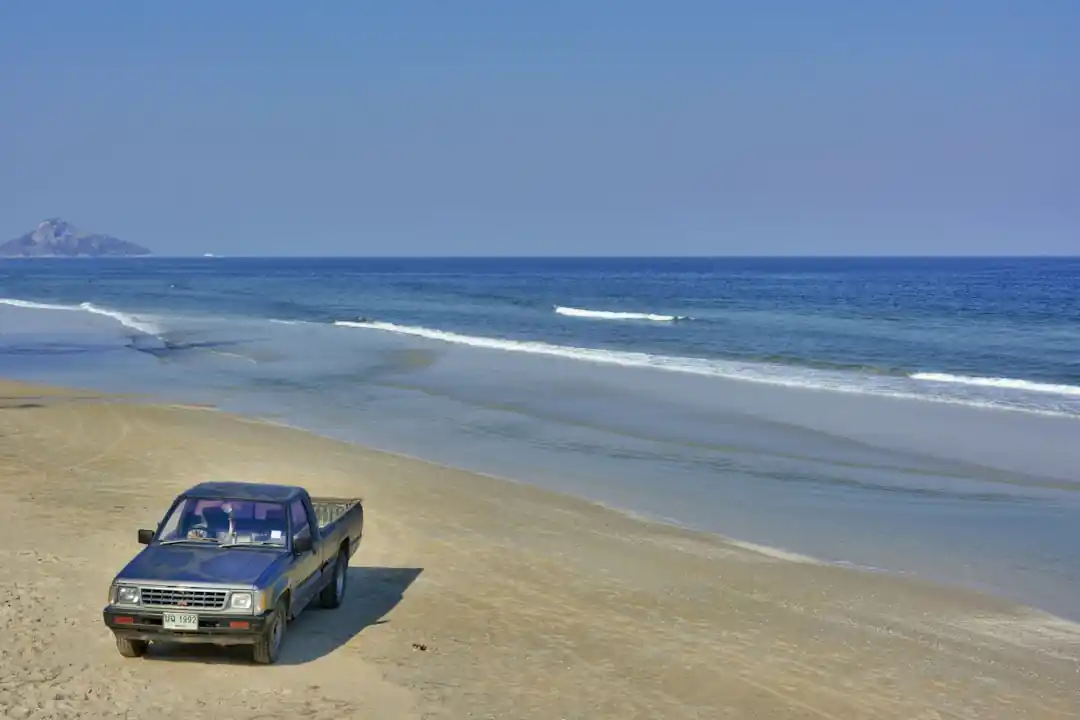夕暮れの砂浜を走る白い車。波打ち際がすぐそばに迫っている。